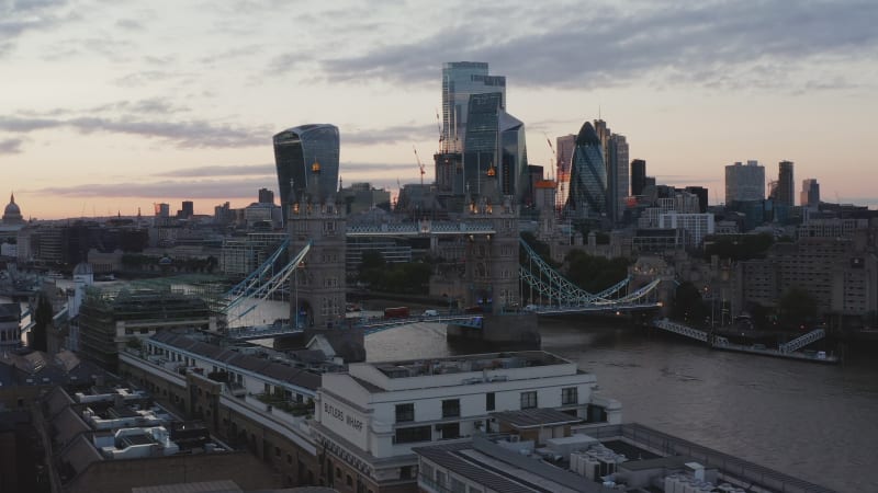 Evening sliding view of Tower Bridge and modern skyscrapers in financial and economical hub. Colourful sunset sky. London, UK