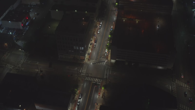 Aerial tilt down footage of cars driving through intersection at night. Streets lit by street lights. Dallas, Texas, US