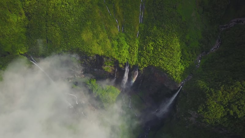 Aerial view above waterfall surrounded by jungle.