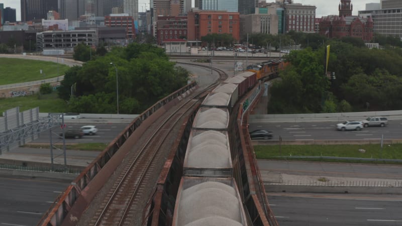 Forwards reveal of freight train standing on track leading on bridge over busy highway. Dallas, Texas, US