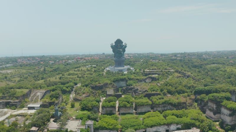 Large statue of Garuda Wisnu Kencana in cultural park in Bali, Indonesia. Forward dolly aerial view of large religious monument surrounded by thick green trees in a park