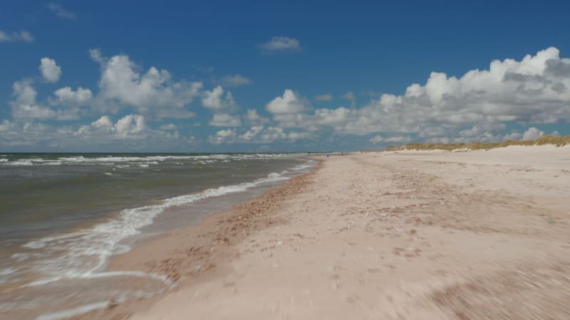 Forwards fly above sea coast. Waves washing sand beach on sunny day.  People enjoying beautiful day at water. Denmark