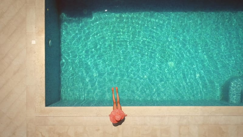 Aerial view of female with hat sitting by swimming pool.