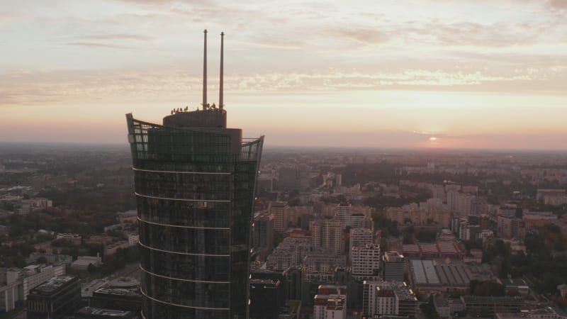 Orbit shot around top of modern futuristic tall building. Warsaw Spire against pink twilight sky. Warsaw, Poland