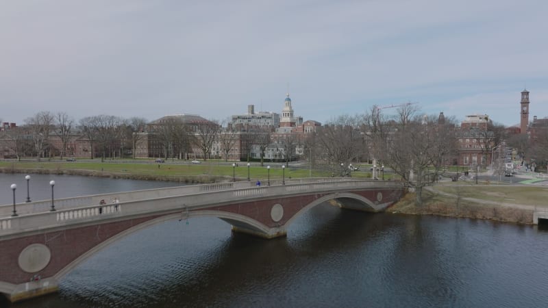 People walking on John W. Weeks Footbridge over Charles river. Revealing buildings in Harvard University campus. Boston, USA