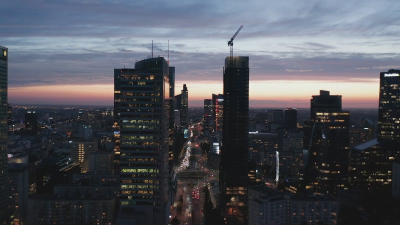 Backwards reveal of downtown skyscrapers. Silhouette of tall office buildings against colourful twilight sky. Warsaw, Poland