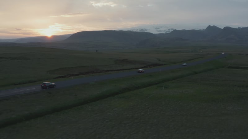 Aerial view drone flight over evening ring road traffic in Iceland. Birds eye of cars driving down straight road through grassy highlands valley at sunset