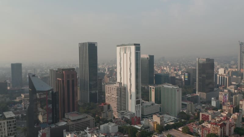 Panorama curve shot of downtown. Flying towards tall office buildings. Limited visibility due to air pollution. Mexico City, Mexico.