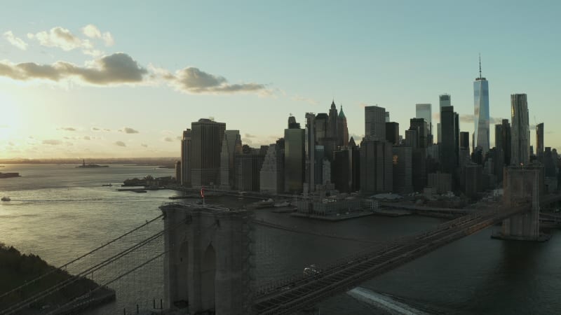 Fly over Brooklyn Bridge with downtown skyline. Silhouettes of office skyscrapers against sunset sky. Manhattan, New York City, USA