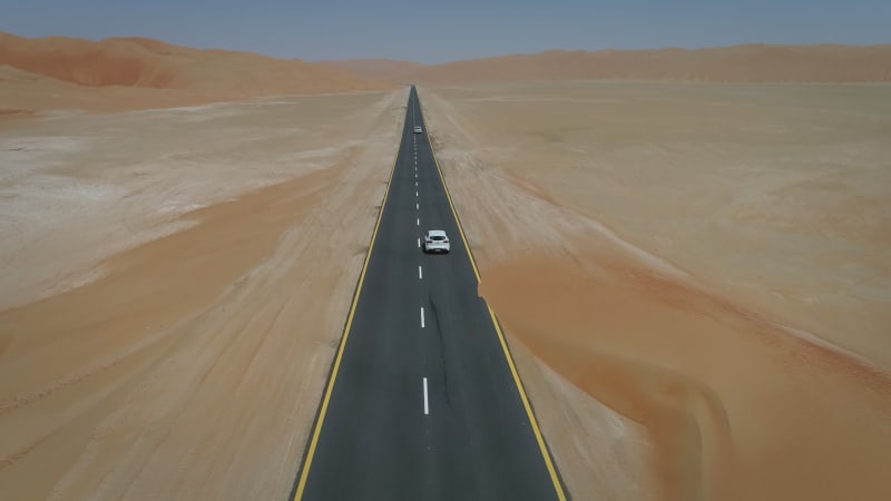 Aerial view of two white car in clean road in the desert.