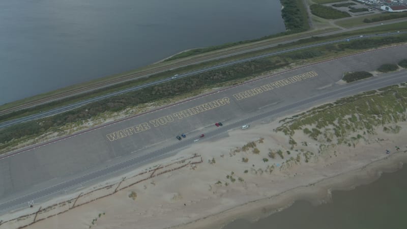 Big Sign on parking lot saying "Water you thinking? Bring in the Dutch!"close to Beach, Aerial Perspective