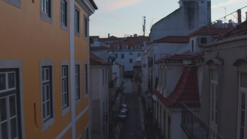 Backwards flying drone camera between buildings in evening downtown. Elevated view of old houses lining narrow streets. Lisbon, capital of Portugal.