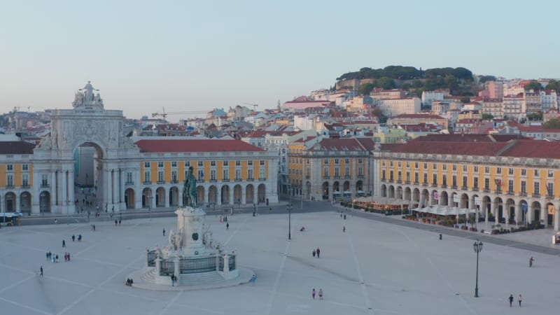 Aerial ascending view of people on Praca do Comercio public square in Lisbon with Arco da Rua Augusta and residential houses in the background