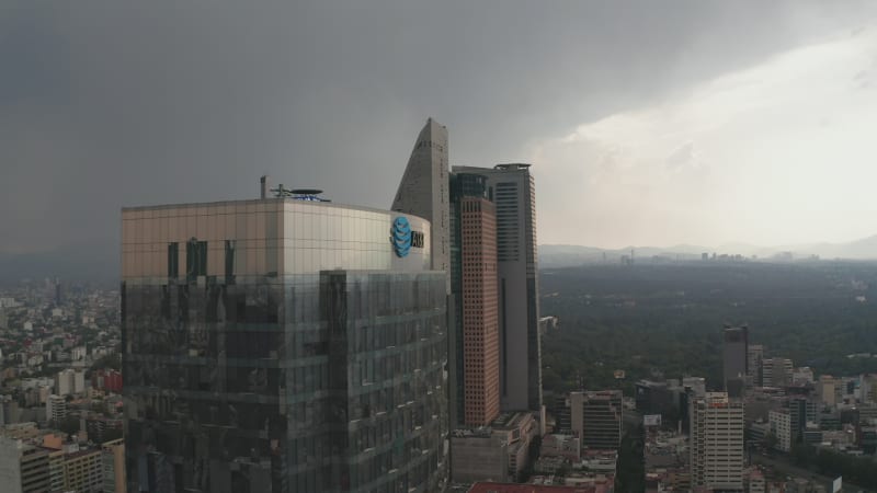 Fly around top of tall office glass modern building. Panning view of cityscape. Dramatic cloudy sky before heavy rain. Mexico City, Mexico.