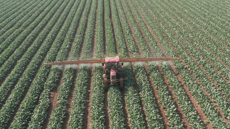 Pesticide Sprayer Tractor working on a large field, Aerial follow footage.