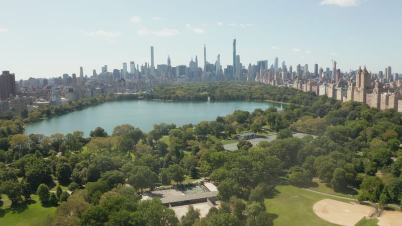 Manhattan Skyscrapers revealing behind beautiful Green Nature with Trees and Lake in Central Park, New York City, Aerial Wide View