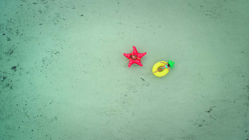 Aerial view of two girls floating on inflatable mattress in transparent sea.