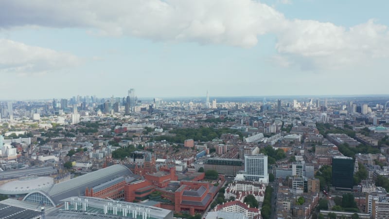 Fly above city. Industrial or commercial buildings around St Pancras train station. Tall modern skyscrapers in background. London, UK