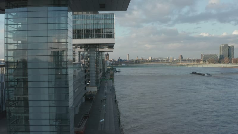 Forwards fly along Rhine river waterfront. Modern residential borough in old harbour. Cargo ship passing under busy bridge. Cologne, Germany