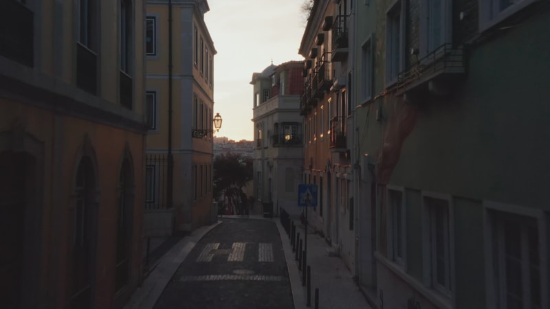 Drone camera flying up through dark narrow street against sunset sky in evening. Lisbon, capital of Portugal.