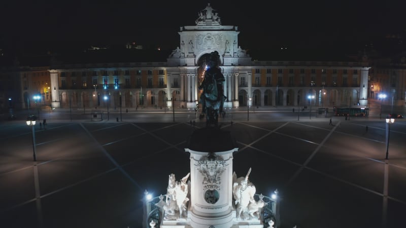 Aerial dolly in night view of Arco da Rua Augusta monument with reveal of street among houses in urban city center of Lisbon, Portugal