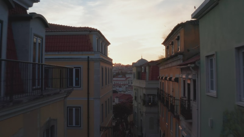 Aerial dolly in reveal of house rooftops and churches in urban city center of Lisbon, Portugal during sunset