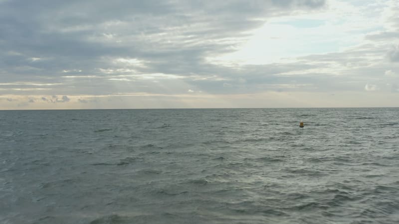 Yellow Buoy in Rough Ocean with Sunset cloudscape in distance, Aerial forward