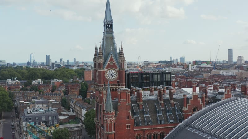 Beautiful decorated brick clock tower as part of old brick St Pancras train station building. Modern downtown skyscrapers in background. London, UK