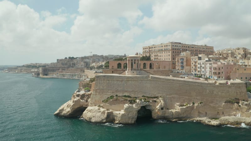 Famous Siege Bell War Memorial in Valletta, Malta capital City, Aerial Drone backwards, Revealing a passing Cargo Ship