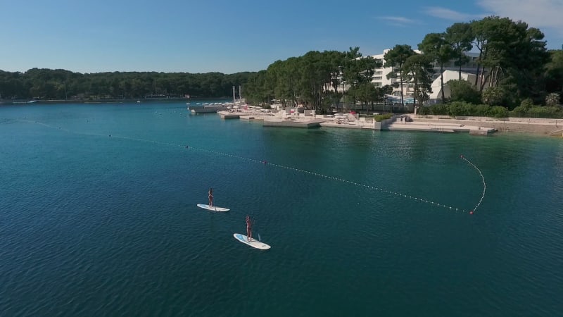 Aerial view of two women practicing stands up board, Losinj coastline.