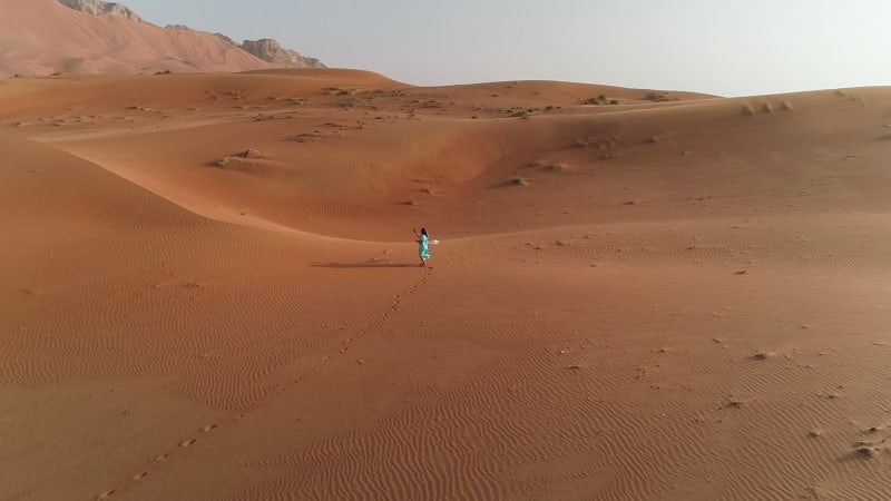 Aerial view of woman walking and making photo in desert.