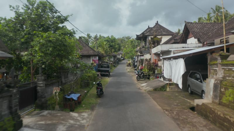 Low flying dolly aerial shot driving down the traditional street in the neighborhood surrounded by residential houses and temples in Bali, Indonesia