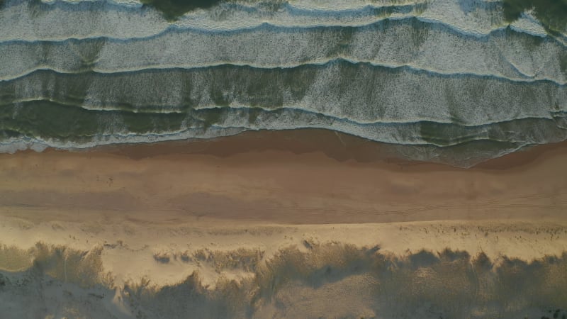 Landscape Wide View of Beautiful Beach with Dunes and Waves Crashing in white foam, Aerial Overhead Top down Birds Eye View, slow sideways