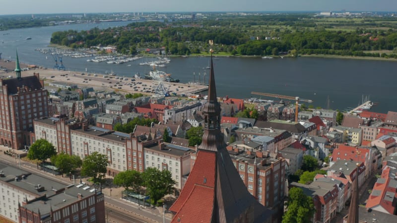 Aerial view of city lying on bank of river. Main wide street with massive buildings. Fly above Saint Marys church red tiled roof and tower