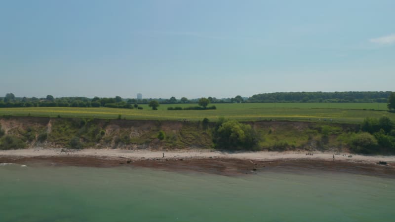 Aerial drone view of vast springtime green countryside field, Baltic sea, Brodten, Germany, backwards, sunny day