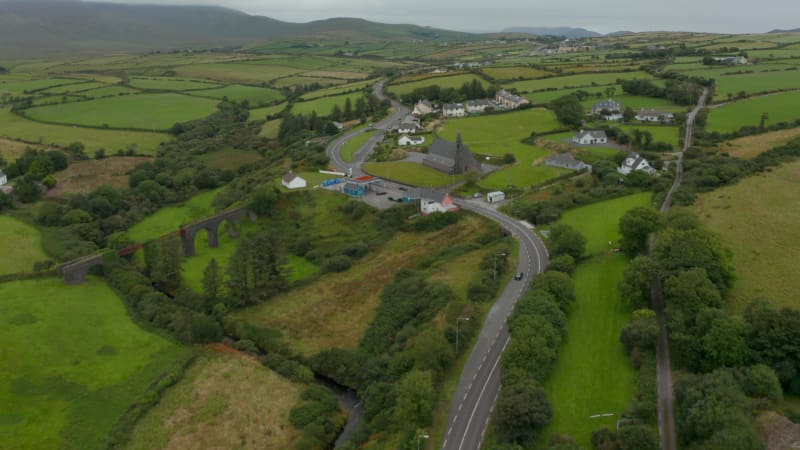 High angle view of road winding through village with sparse housing development. Tilt up reveal of countryside panorama. Ireland