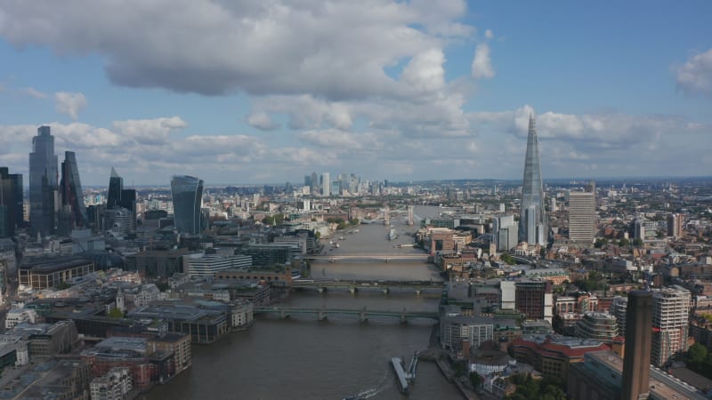 Backwards fly above River Thames, revealing modern skyscrapers in City district, Millennium footbridge and Tate Modern art gallery. Aerial view of city centre. London, UK