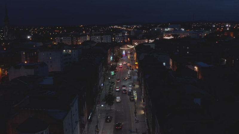 Fly above night city. Cars driving in streets of urban neighbourhood. Light decoration. Limerick, Ireland