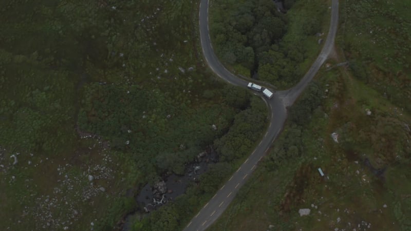 High angle view of vehicle passing through curves on narrow road in countryside. Birds eye shot of van with trailer. Ireland