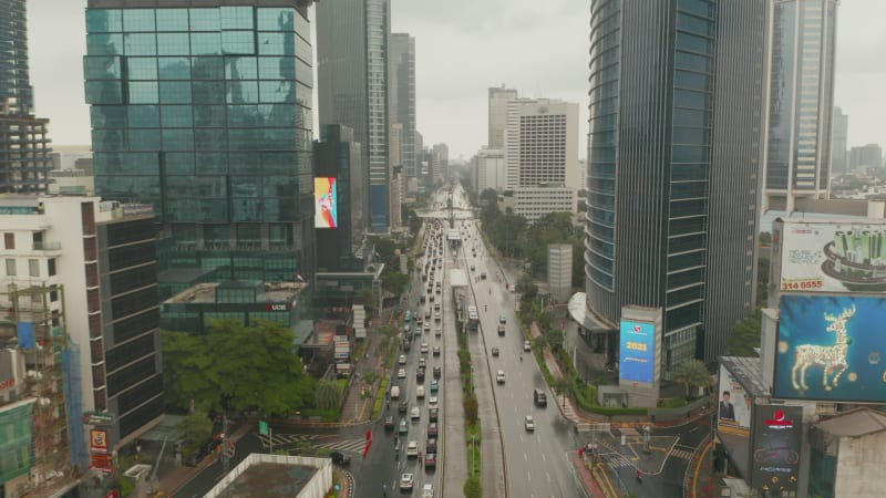 Descending aerial tilt pedestal shot of multi lane traffic and public transportation tram approaching in urban city center of Jakarta