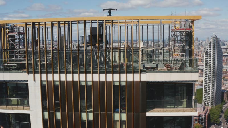 Orbit shot around top of One The Elephant skyscraper. Scaffolding and crane of top platform, repairing of building or doing maintenance. Panoramic view of city. London, UK