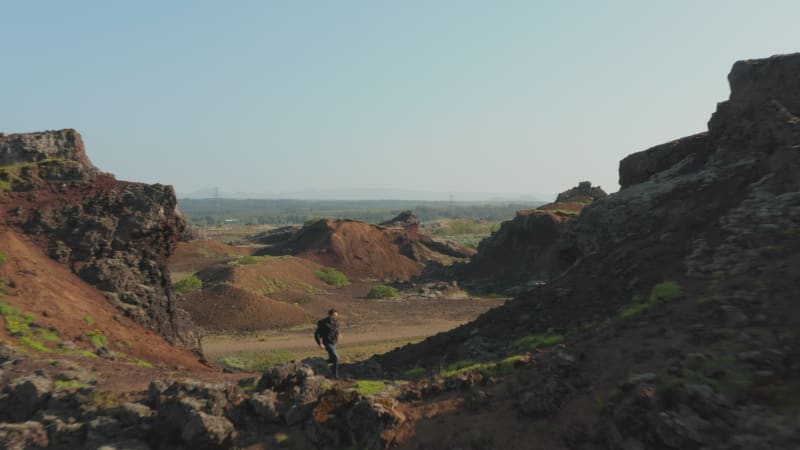 Aerial view of man explorer backpacker running hiking a rock formation in Iceland. Drone view of young man tourist discovering amazing wilderness of desert panorama with stone cliff