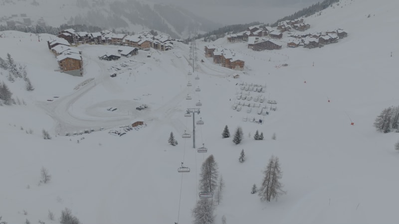 Tilt down and up shot above chair lift snow covered chalets and cars next to empty ski slopes at La Plagne, France at snowing misty morning