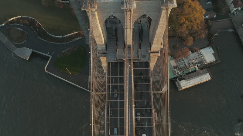 High angle view of cars driving on Brooklyn bridge over river. Tilt up reveal of Suspension tower with US flag on top. Manhattan, New York City, USA