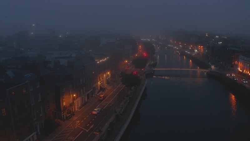 Aerial atmospheric footage of Liffey river waterfront in misty evening. Fly above water surface. Dublin, Ireland