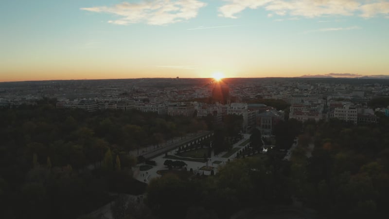 Evening fly above El Retiro Park. Elevated view of decorative Parterre Garden and city against sunset.