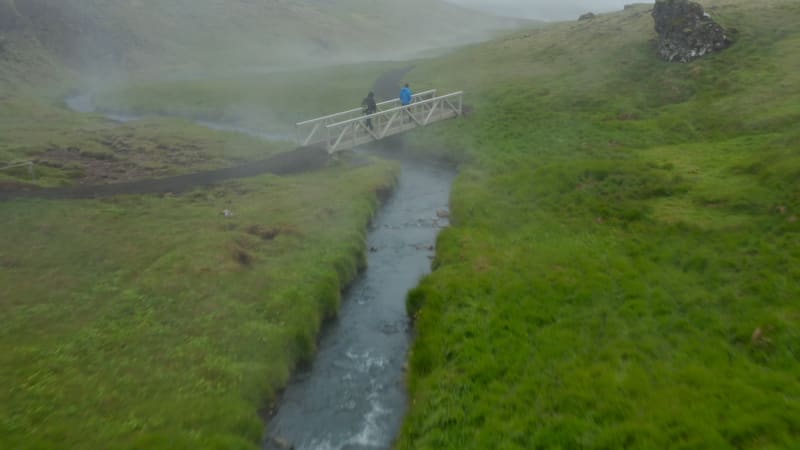 Drone view tourist walking footpath in Reykjadalur Iceland valley in foggy day. Birds eye of hot spring steaming pool in icelandic grassy countryside. Natural spa in Golden Circle