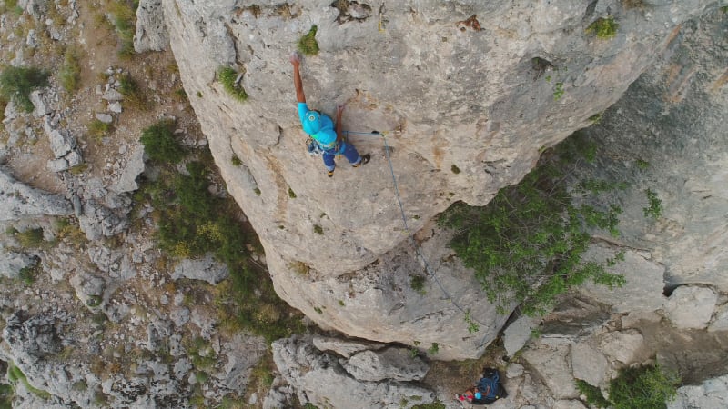 Aerial view of man climbing a stone mountain with safe equipment.