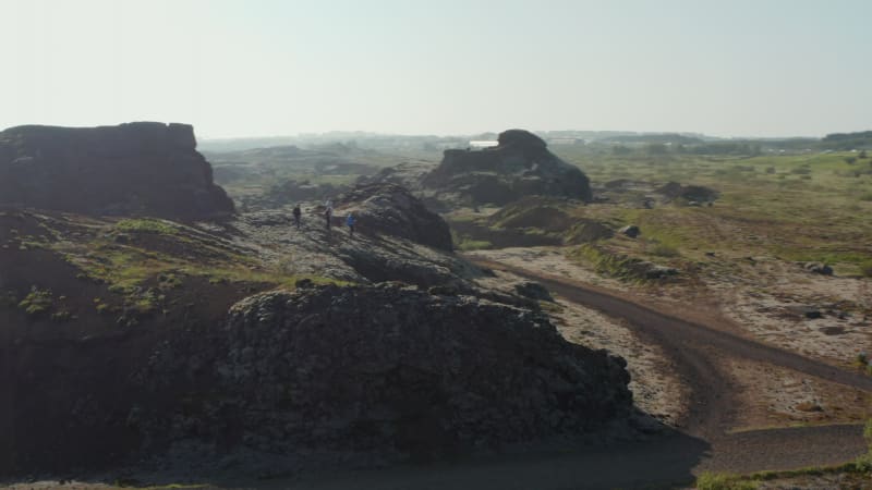 Drone view orbit around group of tourist enjoying panorama climbing hill rock formation in Iceland. Aerial view turning around male explorer discovering amazing in nature