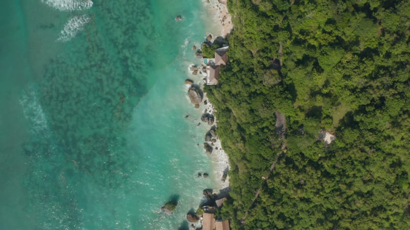 Top down aerial view of luxury tropical villas on Bali coastline. Overhead view of seaside villas and vacation homes by turquoise blue sea in Bali